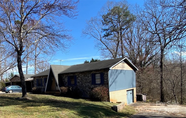 view of side of property with a garage, driveway, a lawn, and stone siding