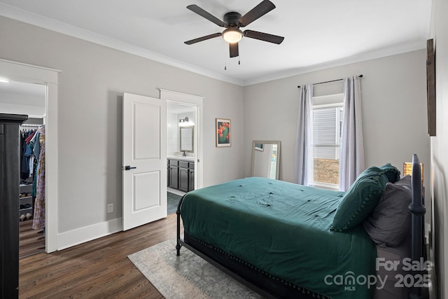 bedroom featuring a walk in closet, crown molding, dark wood-type flooring, baseboards, and a sink