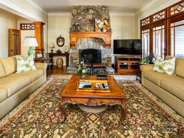 living room with ornamental molding, decorative columns, a stone fireplace, and wood finished floors