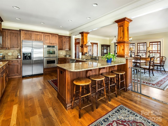 kitchen with decorative columns, dark wood finished floors, light stone counters, a peninsula, and stainless steel appliances