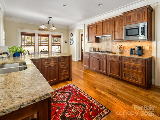 kitchen featuring light wood-style flooring, ornamental molding, a sink, stainless steel appliances, and backsplash