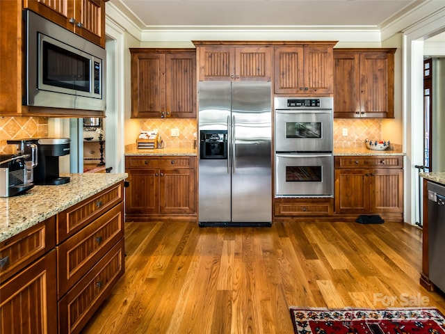 kitchen featuring crown molding, stainless steel appliances, tasteful backsplash, dark wood-type flooring, and light stone countertops