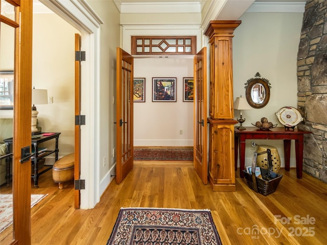 hall featuring light wood finished floors, decorative columns, baseboards, and crown molding