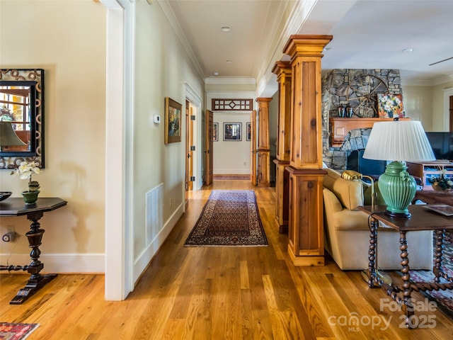 hall featuring visible vents, baseboards, ornamental molding, light wood-type flooring, and decorative columns