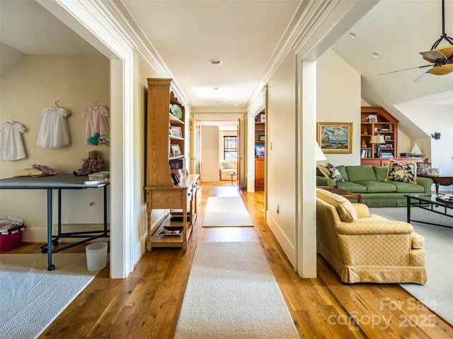 hallway featuring ornamental molding, wood finished floors, built in shelves, and baseboards