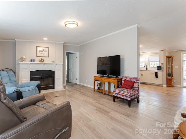 living room with light wood finished floors, crown molding, baseboards, a glass covered fireplace, and a textured ceiling