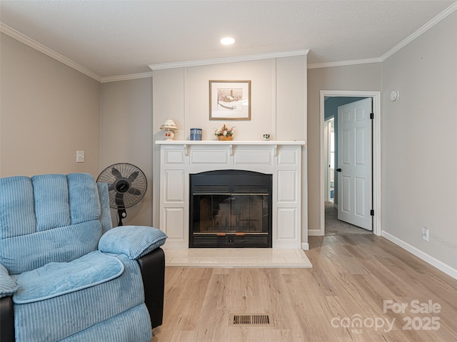 living room with a glass covered fireplace, visible vents, light wood-style floors, and ornamental molding