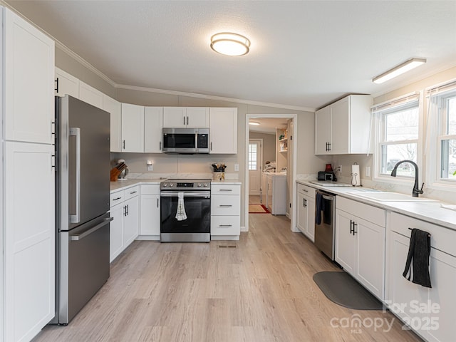 kitchen featuring washer and dryer, stainless steel appliances, ornamental molding, and a sink