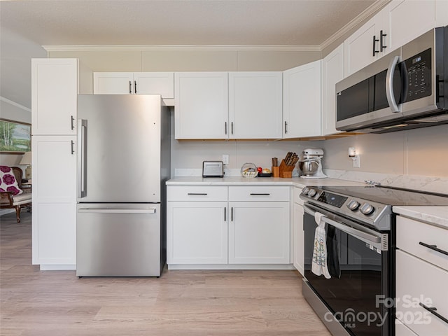 kitchen featuring white cabinetry, stainless steel appliances, light countertops, and ornamental molding