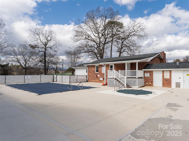 view of front of house featuring a community pool, brick siding, a patio, and fence