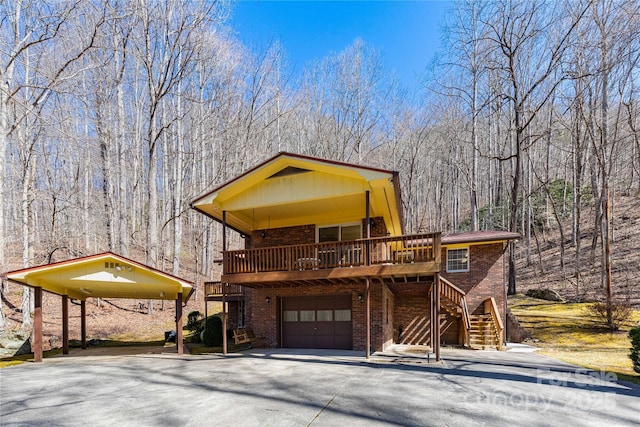 view of front of house with a garage, brick siding, stairs, driveway, and a wooded view