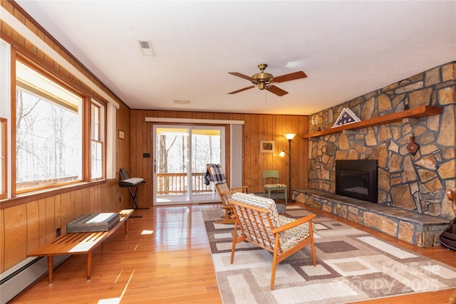 living area featuring light wood-type flooring, wood walls, visible vents, and a stone fireplace