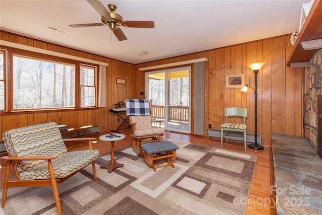 living area featuring a baseboard heating unit, visible vents, ceiling fan, and wood finished floors