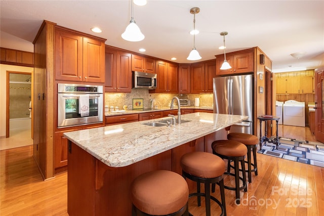 kitchen with tasteful backsplash, stainless steel appliances, light wood-type flooring, separate washer and dryer, and a sink