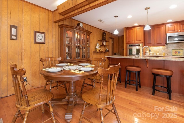 dining area with light wood finished floors, recessed lighting, crown molding, and wood walls