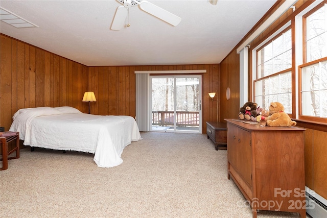 bedroom featuring ceiling fan, a baseboard heating unit, light carpet, wood walls, and access to exterior