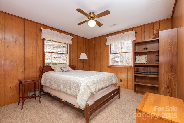 carpeted bedroom with a baseboard radiator, visible vents, ceiling fan, and wooden walls