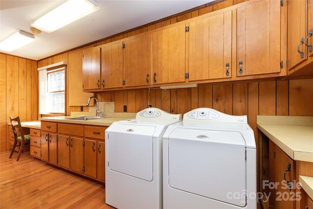 washroom featuring wood walls, a sink, light wood-type flooring, cabinet space, and washing machine and clothes dryer