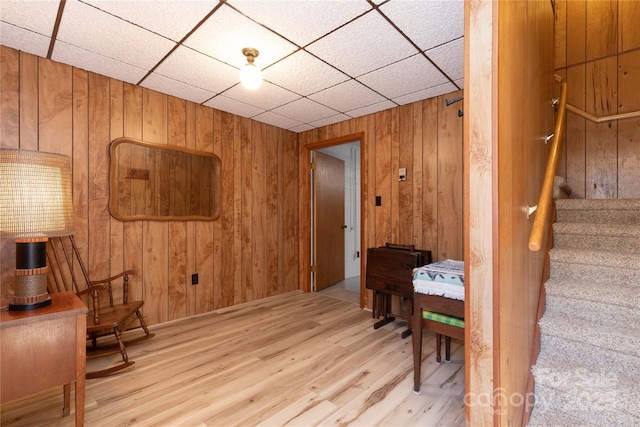 sitting room featuring wooden walls, a paneled ceiling, stairway, and wood finished floors