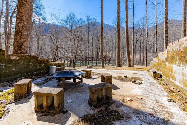 view of patio with a forest view, an outdoor fire pit, and fence