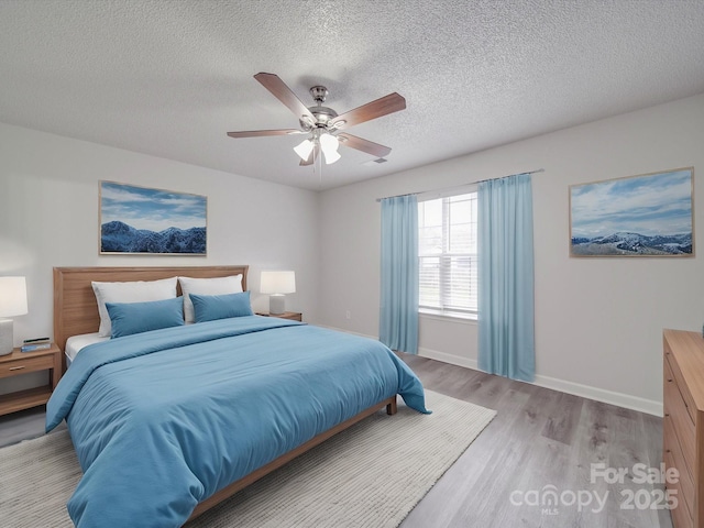 bedroom featuring ceiling fan, a textured ceiling, light wood-style flooring, and baseboards