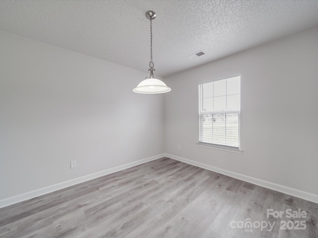 empty room with a textured ceiling, wood finished floors, visible vents, and baseboards