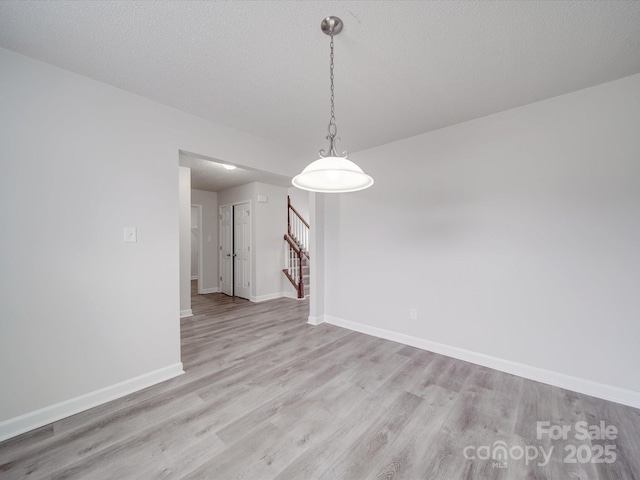 unfurnished room featuring light wood-style floors, stairs, baseboards, and a textured ceiling