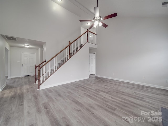 unfurnished living room with visible vents, a high ceiling, wood finished floors, baseboards, and stairs