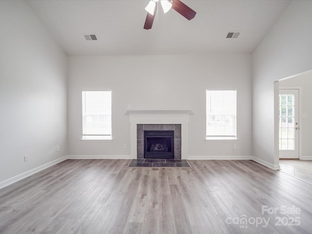 unfurnished living room with ceiling fan, wood finished floors, visible vents, baseboards, and a tiled fireplace