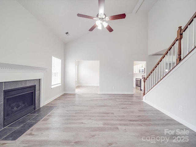 unfurnished living room with stairs, baseboards, a fireplace, and wood finished floors