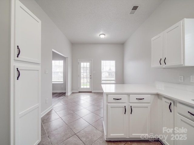 kitchen with a peninsula, light countertops, visible vents, and white cabinetry