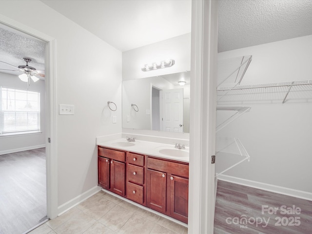 bathroom with double vanity, a textured ceiling, a walk in closet, and a sink