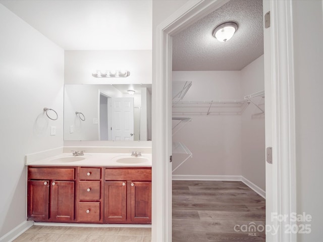 full bath featuring a sink, a spacious closet, a textured ceiling, and double vanity