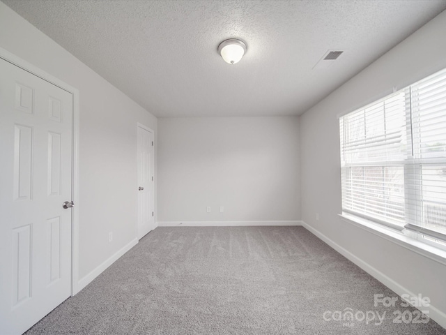 carpeted empty room featuring baseboards, visible vents, and a textured ceiling