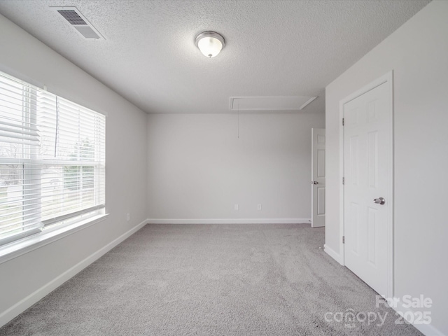 unfurnished room with light colored carpet, visible vents, attic access, a textured ceiling, and baseboards