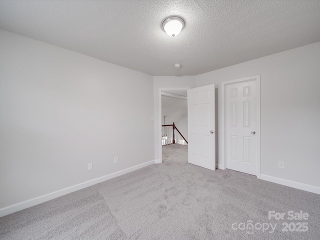 unfurnished bedroom with a textured ceiling, carpet floors, and baseboards