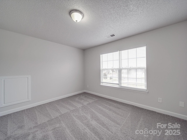 spare room with carpet, a textured ceiling, visible vents, and baseboards