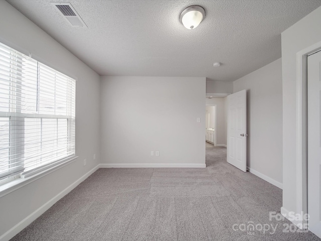 carpeted empty room featuring visible vents, a textured ceiling, and baseboards