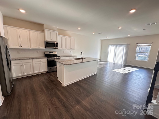 kitchen featuring white cabinets, dark wood finished floors, light stone counters, open floor plan, and stainless steel appliances