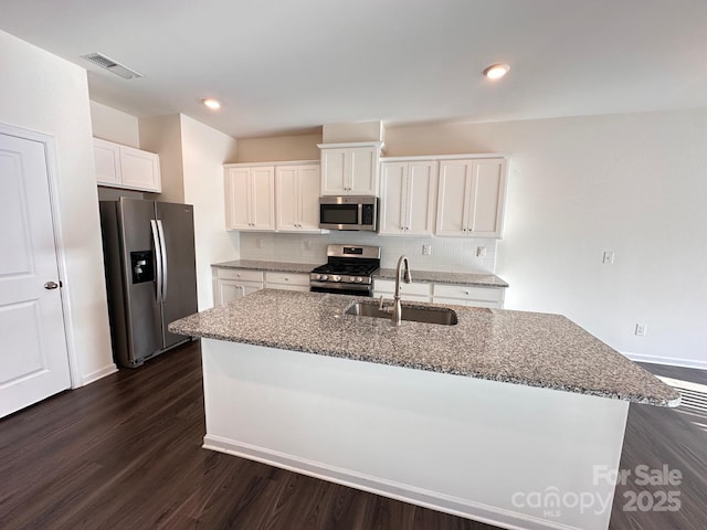 kitchen featuring tasteful backsplash, dark wood finished floors, dark stone countertops, stainless steel appliances, and a sink