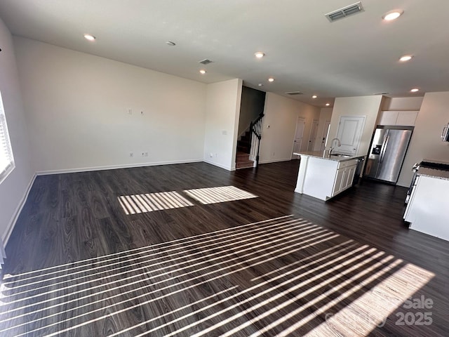 unfurnished living room with visible vents, stairway, dark wood-type flooring, a sink, and recessed lighting