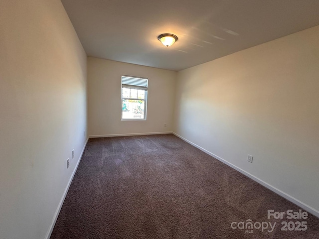 empty room featuring dark colored carpet and baseboards