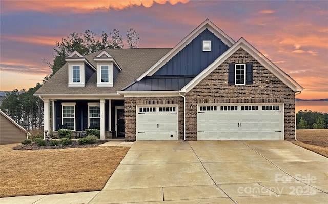 view of front of home featuring covered porch, a shingled roof, concrete driveway, board and batten siding, and brick siding