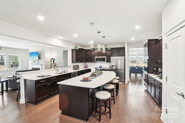 kitchen with a sink, appliances with stainless steel finishes, a breakfast bar area, light countertops, and dark brown cabinets