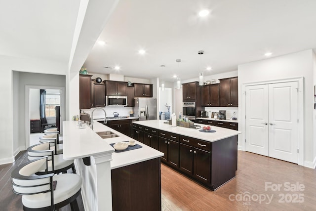 kitchen with a kitchen bar, appliances with stainless steel finishes, a center island with sink, and light countertops