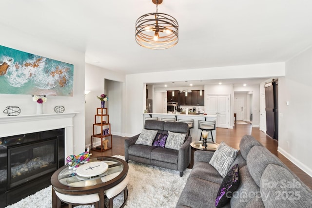 living area with a glass covered fireplace, wood finished floors, baseboards, and a chandelier