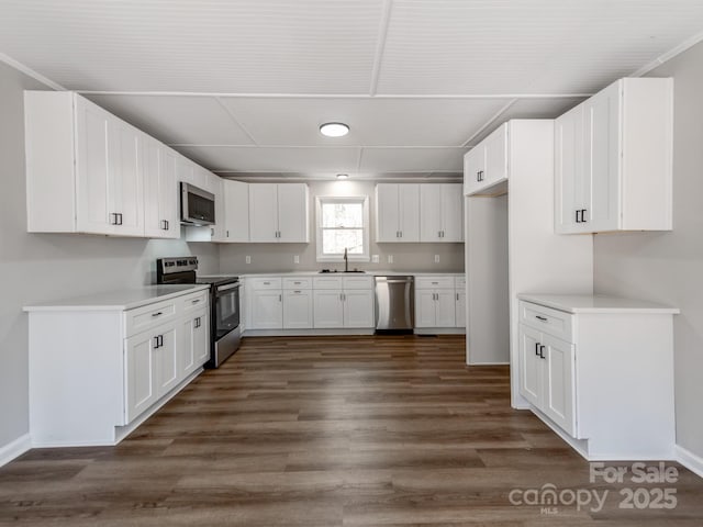 kitchen with stainless steel appliances, dark wood-type flooring, a sink, white cabinets, and light countertops