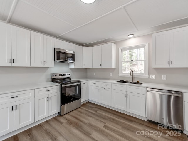 kitchen featuring stainless steel appliances, light countertops, a sink, and light wood-style flooring