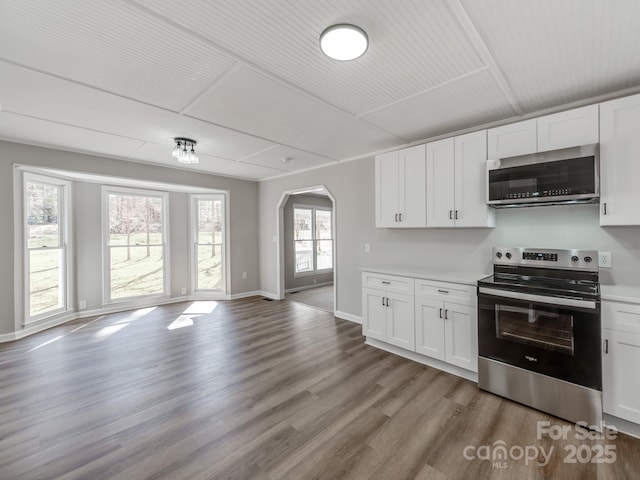 kitchen featuring arched walkways, stainless steel appliances, wood finished floors, white cabinetry, and open floor plan