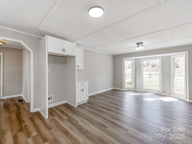 unfurnished living room with arched walkways, ornamental molding, wood finished floors, and baseboards